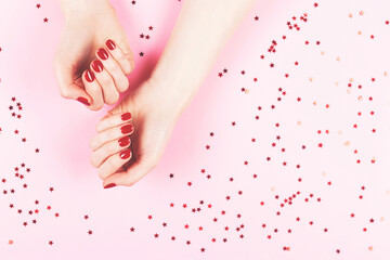 Obraz na płótnie Canvas Manicure and nailcare concept. Two woman hands and falling confetti on pink background. Flat-lay, top view. Copy space.