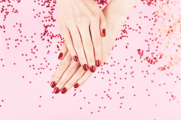 Obraz na płótnie Canvas Manicure and nailcare concept. Two woman hands and falling confetti on pink background. Flat-lay, top view. Copy space.