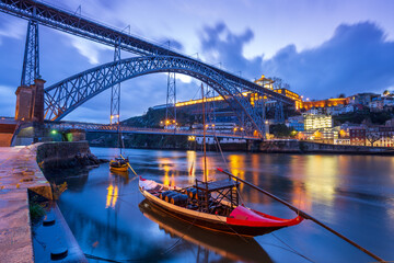 Dawn in Porto, Portugal: The old iron bridge on Douro river, Luis I Ponte, at night, before sunrise. Traditional Portuguese boat used for transporting barrels of port wine in the foreground.