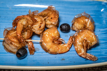 prawns fried in sweet and sour sauce and decorated with olives on a blue plate