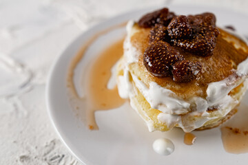 A stack of crumpets and pancakes with sour cream and strawberry sweet jam with berries on top of the dish. Dessert on a white plate with fruit in the background