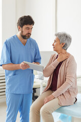 Obraz premium Senior woman has a visit at doctor's office she complaining on the pain in her neck while doctor using tablet pc