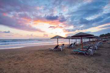 Empty beach with umbrellas and deck chairs closed. Unbelievable sunrise. 2020 summer quarantine travel. Beautiful summertime view seascape. Relax places island Crete, Greece.