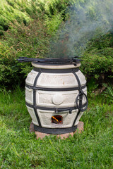 Burning smoking tandoor stands on the grass.