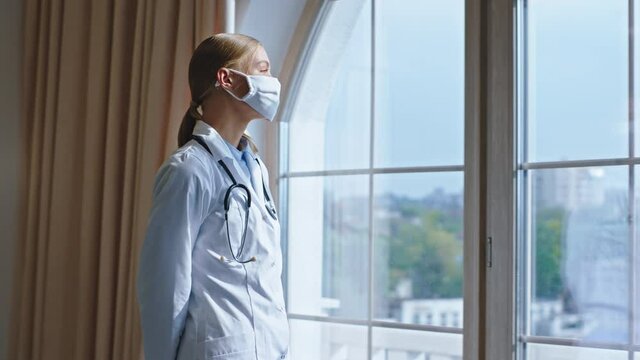 Beautiful Young Woman Doctor With A Protective Mask She Take A Break Looking Through The Panoramic Window And Thinking. Shot On ARRI Alexa Mini