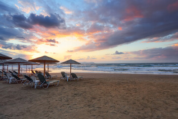 Empty beach with umbrellas and deck chairs closed. Unbelievable sunrise. 2020 summer quarantine travel. Beautiful summertime view seascape. Relax places island Crete, Greece.