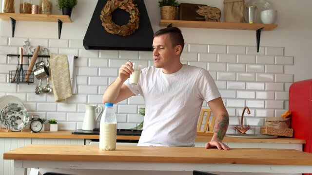 Young man drinking milk in kitchen. Adult male enjoying useful drink for breakfast.