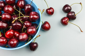 Obraz na płótnie Canvas Red organic ripe cherries on a pink bowl and on a light blue background