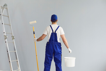 Back view of home repair worker holding roller brush and bucket with paint. Professional contractor...