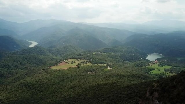 Aerial panning shot of river on green landscape against cloudy sky, drone flying over forest - Tavertet, Spain