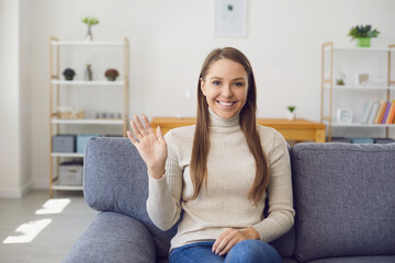 Young woman looking at the camera waving her hand online while having a laptop of call connection...