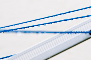 Blue clothing lines of a clothes spin with many raindrops at the string in front of a light background, after the rain. Retro way of doing the laundry.