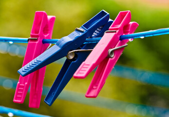 A blue clothing line with many raindrops at the string in front of a dark  background, with two pink and a blue peg after the rain. Retro way of doing the laundry.