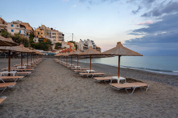 Fototapeta na wymiar Empty beach with umbrellas and deck chairs closed. Unbelievable sunrise. Beautiful summertime view seascape. 2020 summer quarantine travel. Relax places island Crete, Greece.