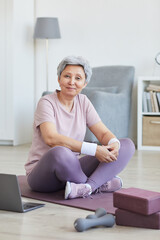 Portrait of senior woman sitting on exercise mat and looking at camera she training at home