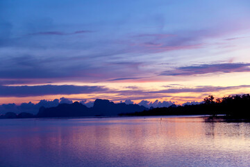 Fototapeta premium Beautiful purple pink sunset sky with dark clouds on tropical summer evening twilight horizon over calming sea water surface & calm ocean wave at island paradise 