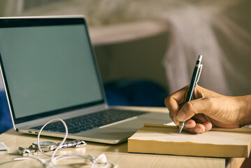 Concept wrok from home man's hand is writing something and using a laptop at his home