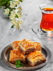 Turkish (eastern) dessert Ramadan Baklava with walnuts and hazelnuts, black strong Turkish tea in a glass of armudu (boomaly). Close-up, shallow depth of field, spring still life