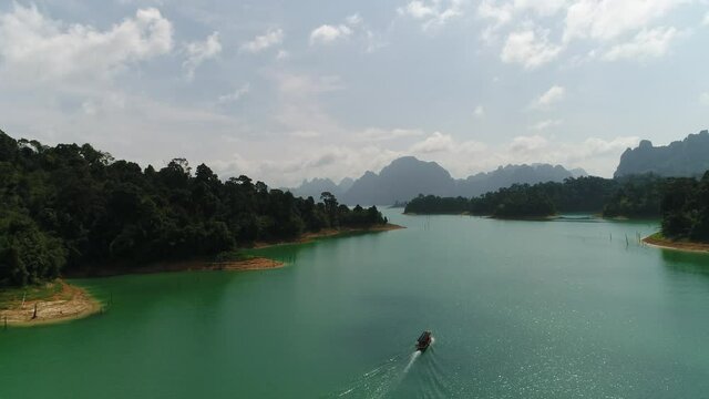 Video footage of the back of a small boat with a flag sailing in the strait. Shores are visible on both sides, on the banks of a dense forest. On the horizon are the outlines of mountains, hills, clou