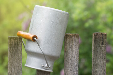 An aluminum pot hangs on an old fence. Dishes for milk and other drinks. Life in the village.