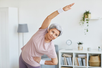 Portrait of senior woman in sports clothing doing exercises in the living room at home