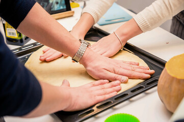 Hands of a man and a girl put the dough on a baking sheet. Cooking pizza with the whole family