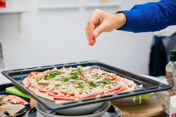 The man's hand sprinkles spices on the pizza. The cook adds seasoning to the pie