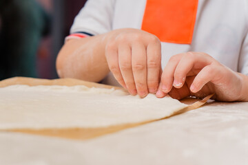 The child's hands make a pizza base out of dough. Kid's cooking class on baking