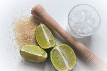 Fototapeta na wymiar lime, cane sugar, pestle and crushed ice on a white table, ingredients for preparing a cocktail