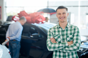 Smiling man posing near car with arms crossed.