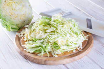 Sliced fresh cabbage on a cutting board with a grater on a wooden background