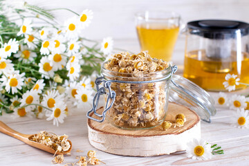 Dried chamomile in the jar on the wooden table. Organic Chamomile Tea in cup and flowers
