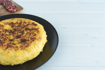 Potato omelette on a black plate on a white background. Copy space.