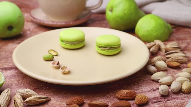 male hand picks green macaroons from a ceramic plate on a brown concrete background. Side view, close up.