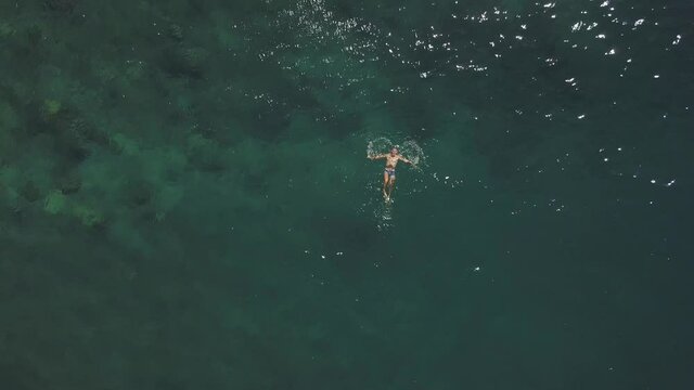 A fit young man enjoys swimming anf floating in the blue ocean at summer.