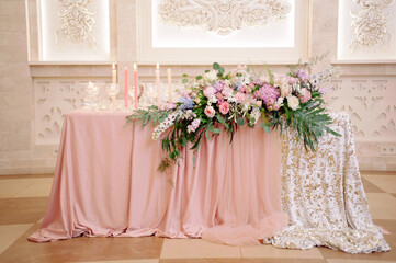Wedding party. Newlyweds table decorated with tender pink tablecloth, candles and elegant floral composition. Stylish decoration on table.