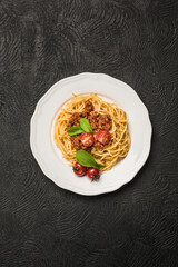 Delicious classic Italian Bolognese pasta with tomatoes and Basil on a plate on a dark background.