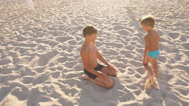 Happy little boy running around the white sand beach is about a teenage brother in the setting sun, slow motion video. Children play catch-up on the snow-white sand at sunset.