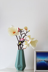 fabric magnolia in a decorative vase against a white background, next to it one of my pictures in the harbour of Heiligenhafen in Germany