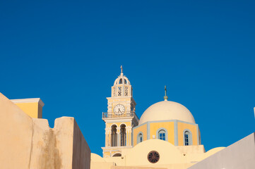 Church dome and clock tower in a Mediterranean style against a bright blue sky