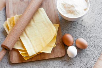 Ingredients for homemade lasagna. Rolling pin, flour, eggs and fresh lasagna sheets. Selective focus. Top view