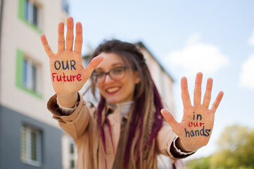 Modern girl with long dreadlocks and eyeglasses in nude color trench is showing hands with written...