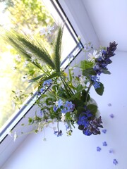 Bunch of wild flowers in a transparent vase on a white windowsill