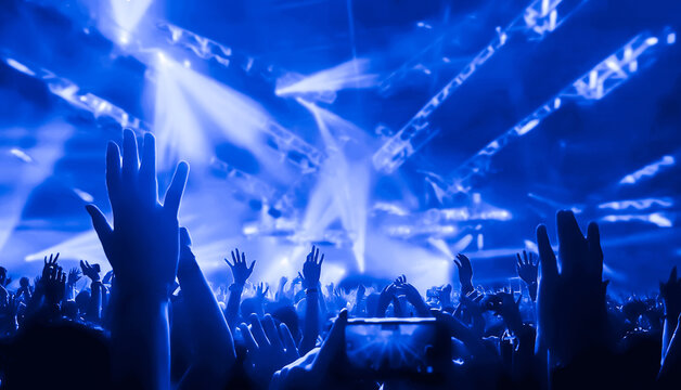 Happy people dance in nightclub DJ party concert and listen to electronic dancing music from DJ on the stage. Silhouette cheerful crowd celebrate New Year party 2020. People lifestyle DJ nightlife.