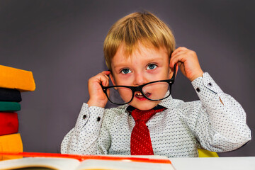 cute boy with glasses sitting at a Desk. Blond nerd with glasses.