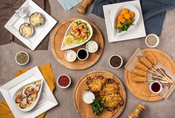 Table with an assortment of hot snacks: mushroom julienne, shrimps with sauces, fried cheese, potato balls, baked vegetables, potato pancakes.