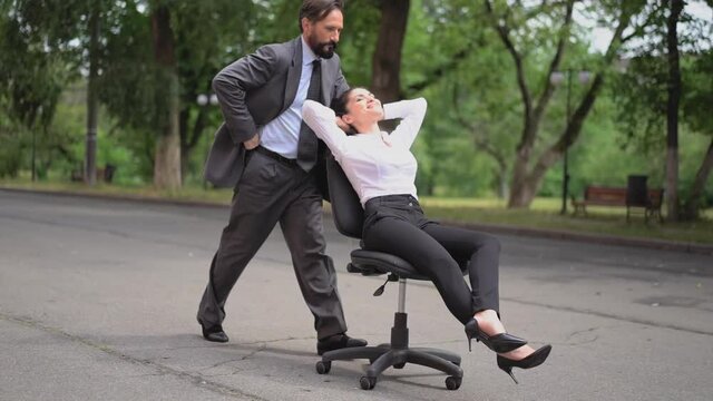 A man pushes a chair with a girl boss on the street in which scoffs at employees. The girl makes employees entertain her. Harassment at work. Prores 422. 