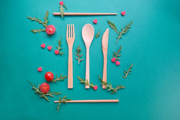 Up view of wood ecologic cutlery with 
rocket salad, tomatoes and red little hearts. Green background. Concept of healthy and vegan alimentation.
