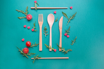 Up view of wood ecologic cutlery with 
rocket salad, tomatoes and red little hearts. Green background. Concept of healthy and vegan alimentation.