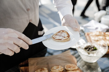 Obraz na płótnie Canvas The waiter smears the pancake with butter on a white plate.